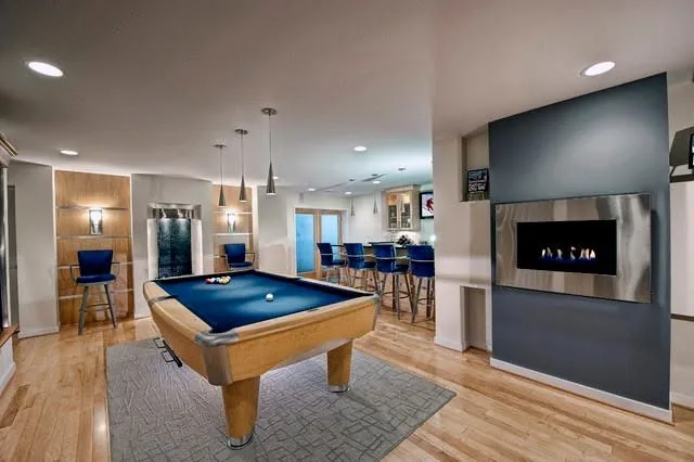 Finished basement with pool table, bar seating, pendant lights, and modern fireplace