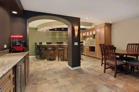 Finished basement bar and dining area with stone-look tile floor, dark archway, and wood cabinetry
